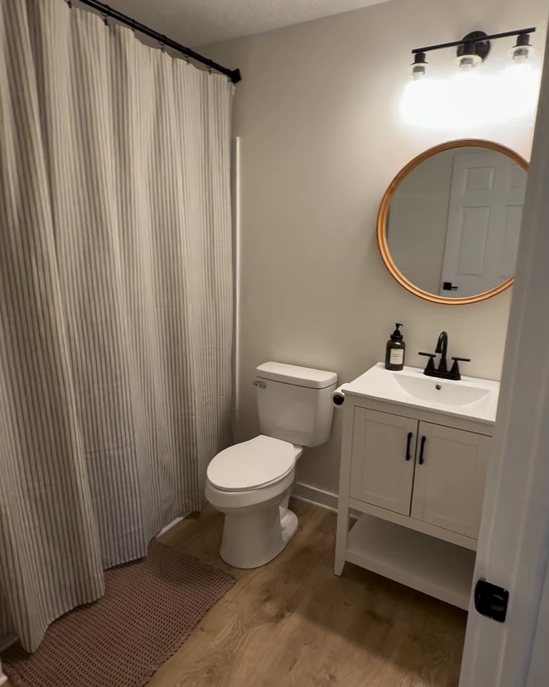 Finished home addition bathroom with a white vanity, round mirror, black fixtures and a striped shower curtain
