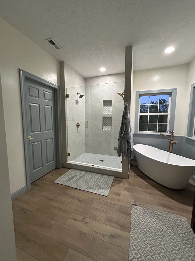 Remodeled bathroom with a glass walk-in shower with tiled niches and a freestanding tub